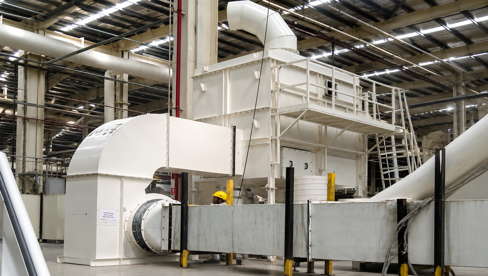 Large industrial air pollution control system with ducting, centrifugal blower, and filtration equipment installed inside a manufacturing facility.